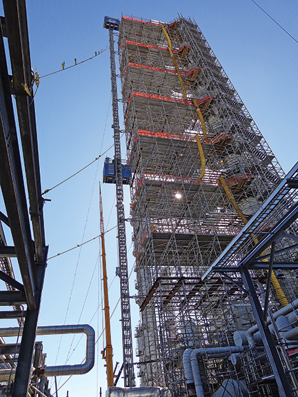 A tall industrial structure with scaffolding and safety netting, showcasing industrial contractor services under a clear blue sky.