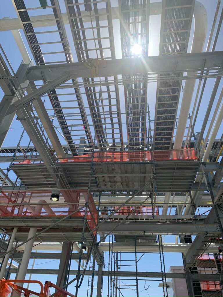 Steel scaffolding and metal framework of a building under construction by industrial building contractors, sunlight shining through overhead.