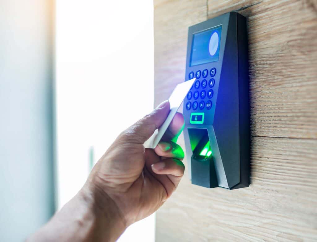A person holds a key card up to an electronic keypad access control system, commonly used by industrial building contractors.